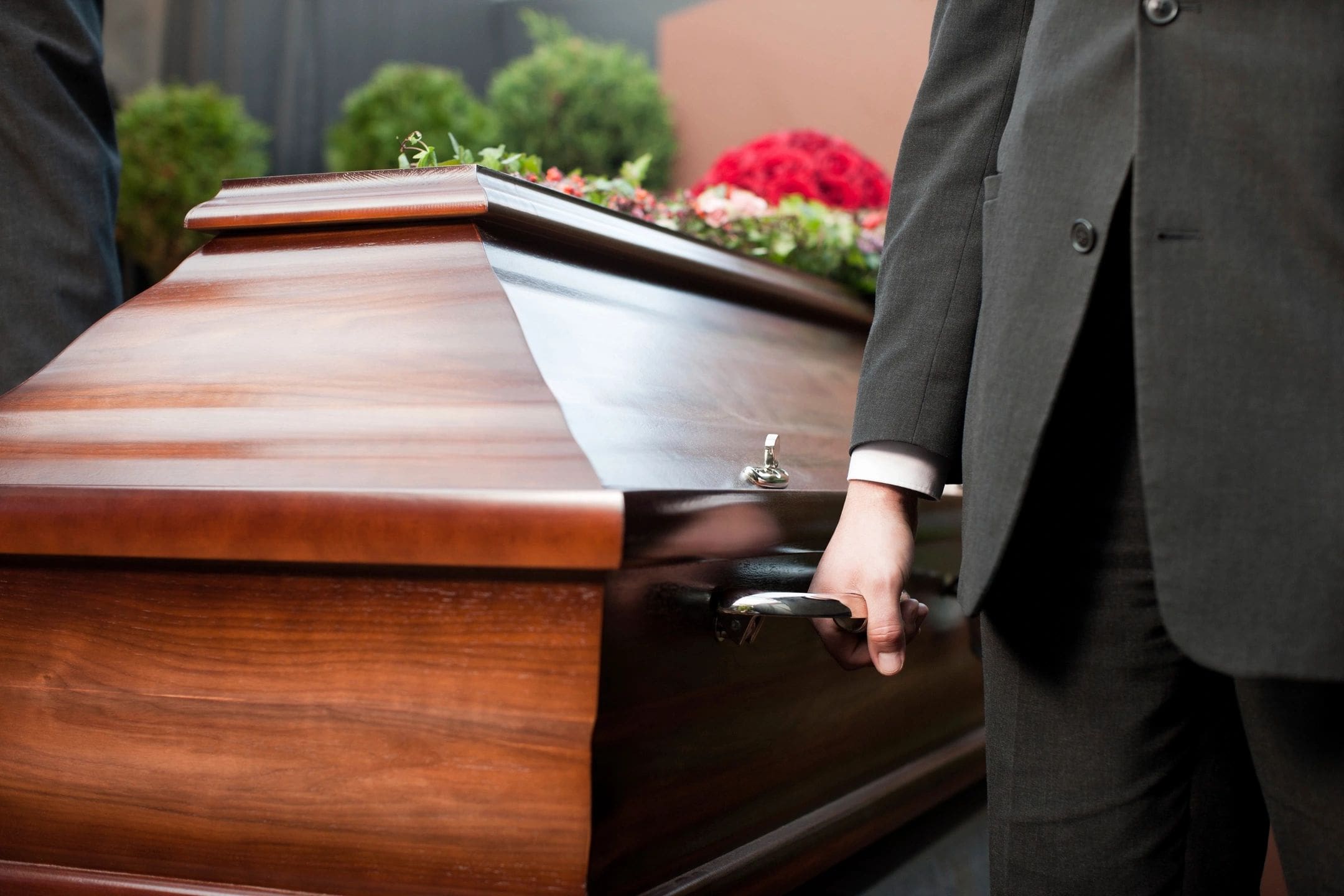 A person in suit and tie standing next to a wooden casket.