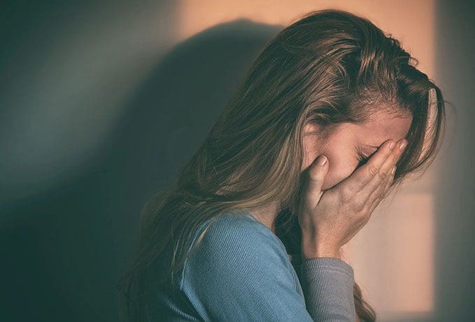 A woman is holding her head in front of her face.