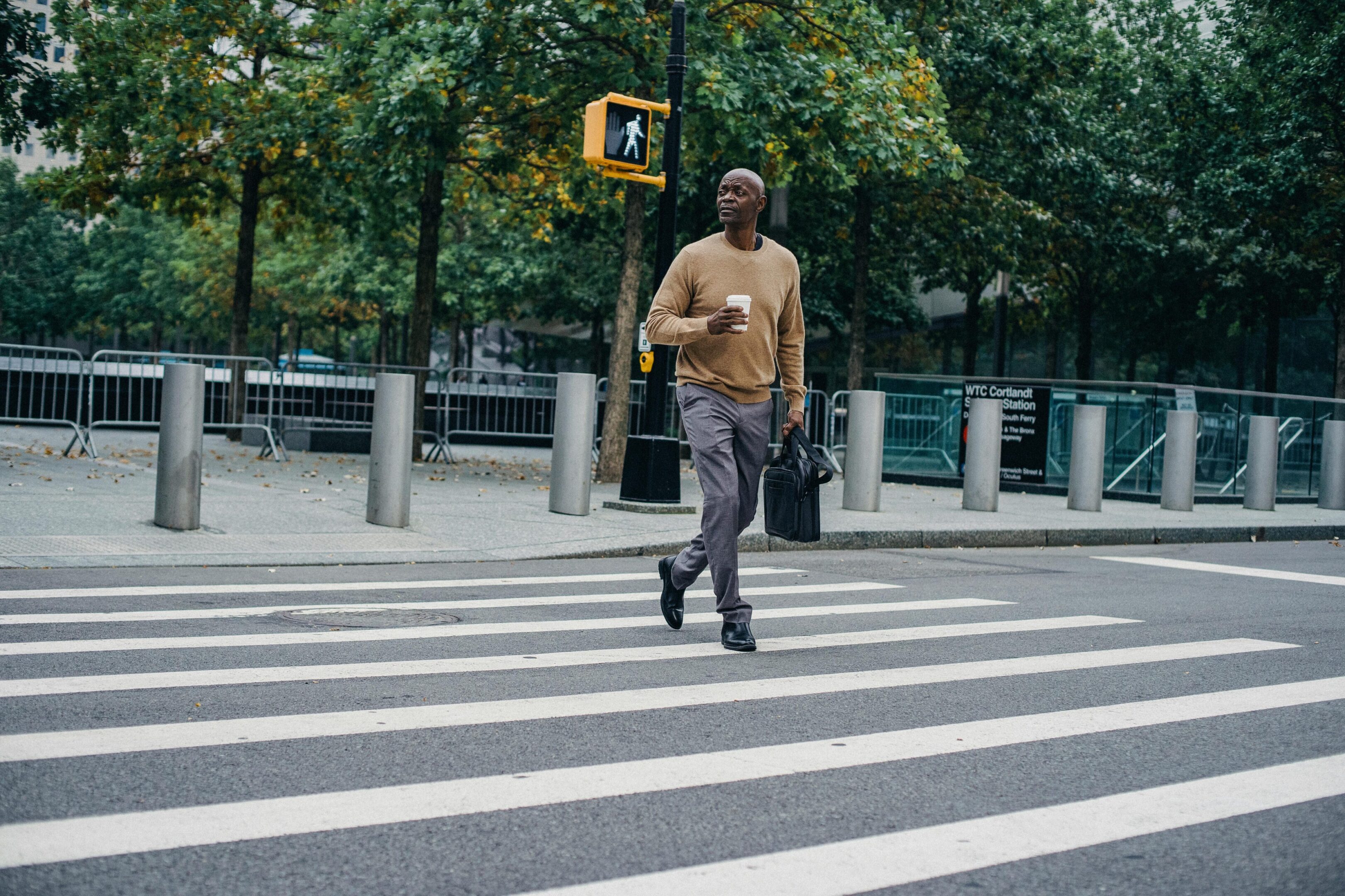 A man is walking across the street in front of a traffic light.